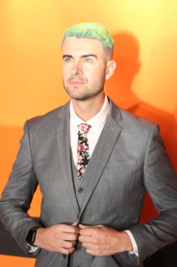 Turuncu arka planda duran yeşil saçlı zarif yakışıklı adam.