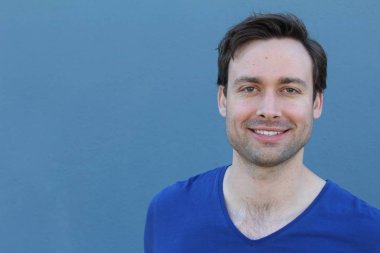 Mavi duvarın önünde sıradan giyinmiş yakışıklı bir gencin yakın plan portresi.