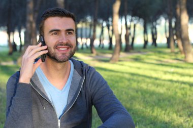 Yeşil Park 'ta telefonla konuşan sıradan giyinmiş yakışıklı genç adamın yakın plan portresi.