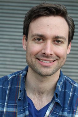 Gri duvarın önünde sıradan giyinmiş yakışıklı bir delikanlının yakın plan fotoğrafı.