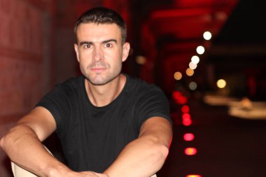 Geceleri sokakta siyah tişörtlü yakışıklı bir adamın yakın plan portresi.