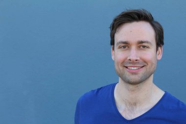 Mavi duvarın önünde sıradan giyinmiş yakışıklı bir gencin yakın plan portresi.