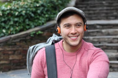 Yakından çekilmiş bir portre, günlük giysiler içindeki yakışıklı genç adam klasik kulaklıklarla müzik dinliyor ve şehir sokaklarında oyuncu.