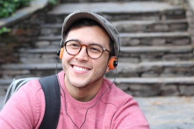 Yakından çekilmiş bir portre, günlük giysiler içindeki yakışıklı genç adam klasik kulaklıklarla müzik dinliyor ve şehir sokaklarında oyuncu.