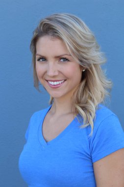 Mavi arka planda gülümseyen güzel sarışın kızın yakın plan portresi.