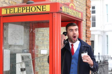 Yakışıklı genç işadamının yakın plan portresi. Elinde kağıt bardak kahve ile sokakta telefon kulübesinde konuşuyor.