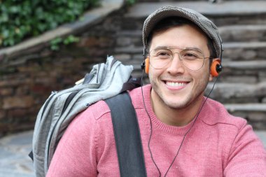 Yakından çekilmiş bir portre, günlük giysiler içindeki yakışıklı genç adam klasik kulaklıklarla müzik dinliyor ve şehir sokaklarında oyuncu.