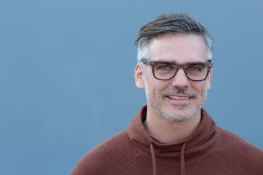 Mavi duvarın önünde kapüşonlu, yakışıklı, olgun bir adamın yakın plan fotoğrafı.