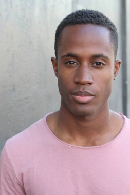 Gri duvarın önünde pembe tişörtlü yakışıklı genç adamın yakın plan portresi.