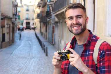 Eski şehir caddesinde sırt çantalı ve klasik kameralı yakışıklı bir gencin yakın plan portresi.