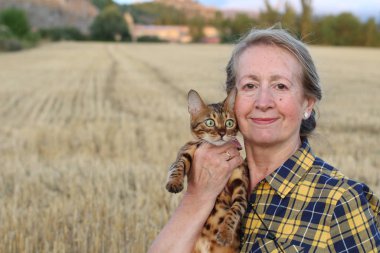Yaşlı kadın elinde şirin bir kedi tutuyor, gündüzleri kuru tarlada duruyor. 