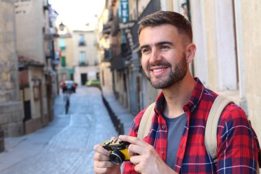 Eski şehir caddesinde sırt çantalı ve klasik kameralı yakışıklı bir gencin yakın plan portresi.