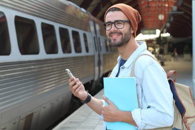 Yakından bakınca, tren istasyonunda akıllı telefonlu sıradan giysili yakışıklı bir gencin portresi.