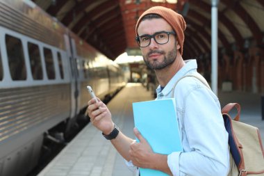 Yakından bakınca, tren istasyonunda akıllı telefonlu sıradan giysili yakışıklı bir gencin portresi.