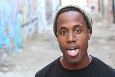 Dilinde hap olan yakışıklı Afro-Amerikan bir adamın sokakta dikilen portresi.