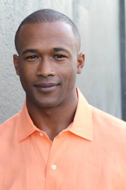 Gri duvarın önünde sıradan giysiler içinde yakışıklı Afro-Amerikan bir adamın yakın plan portresi.