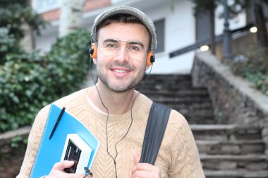 Yakından çekilmiş bir portre, günlük giysiler içindeki yakışıklı genç adam klasik kulaklıklarla müzik dinliyor ve şehir sokaklarında oyuncu.