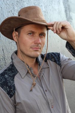 Gri duvarın önünde kovboy şapkalı yakışıklı genç adamın yakın plan portresi.