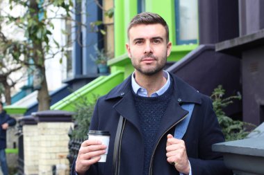Sokakta elinde kağıt bardak kahveyle ceketli yakışıklı bir gencin yakın plan portresi.