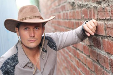 Duvara yaslanmış kovboy şapkalı yakışıklı genç adamın yakın plan portresi.