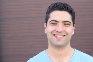 close-up portrait of handsome young man in blue t-shirt in front of brown wall
