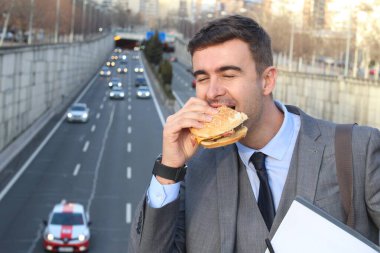 close-up portrait of handsome young businessman in suit eating burger on street