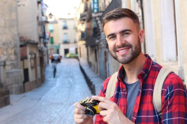 Eski şehir caddesinde sırt çantalı ve klasik kameralı yakışıklı bir gencin yakın plan portresi.
