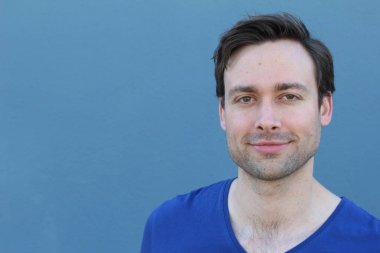 Mavi duvarın önünde sıradan giyinmiş yakışıklı bir gencin yakın plan portresi.