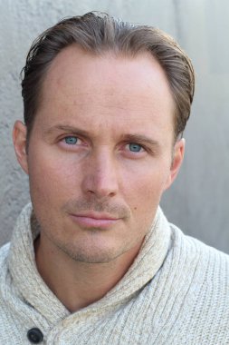 Gri duvarın önünde kazaklı yakışıklı genç adamın yakın plan portresi.