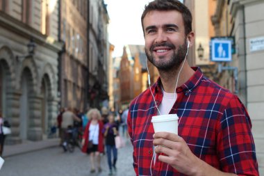 Sokakta elinde kağıt kahve olan yakışıklı bir gencin yakın plan portresi.