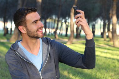 Parkta akıllı telefon kullanan yakışıklı bir gencin yakın plan portresi.