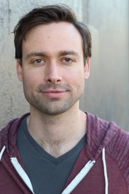 Gri duvarın önünde sıradan giyinmiş yakışıklı bir gencin yakın plan portresi.