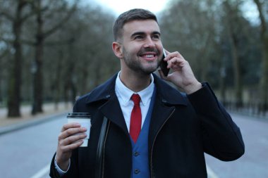 Takım elbiseli ve ceketli yakışıklı genç işadamının kağıt bardak kahveyle yakın plan portresi.