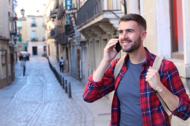 Sırt çantalı yakışıklı genç adamın eski şehir caddesinde telefonla konuşurken yakın plan portresi.