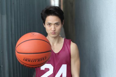 Pembe gömlekli yakışıklı ve sokakta basketbol topu olan Asyalı bir adamın yakın plan portresi.