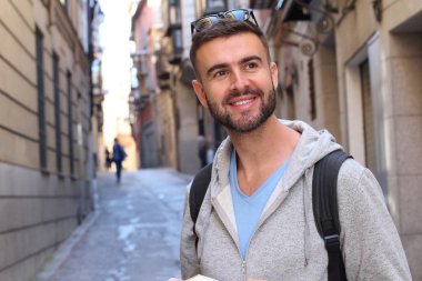 Sırt çantalı ve kitaplı yakışıklı genç adamın şehir sokaklarındaki yakın plan portresi.