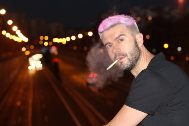 Akşam sokakta sigara içen pembe saçlı yakışıklı genç adamın yakın plan fotoğrafı.