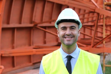 İnşaat alanında koruyucu yelek giymiş yakışıklı bir mimarın yakın plan portresi.