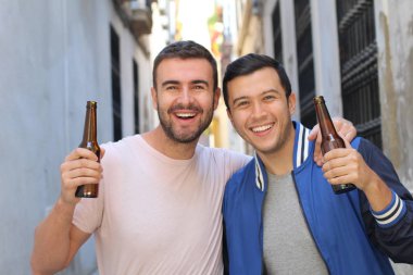İki adam dışarıda soğuk, ferahlatıcı bir birayla tezahürat yapıyor.