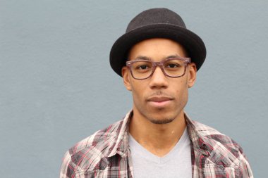 Gri duvarın önünde ekose gömlekli ve şapkalı yakışıklı Afro-Amerikan bir adamın yakın plan portresi.