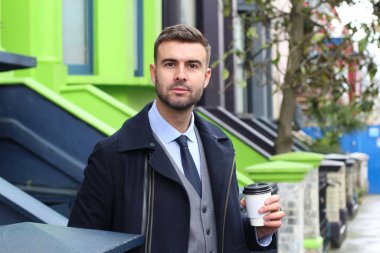 Yakışıklı genç iş adamının yakın plan portresi. Sıcak palto ve sokakta bir fincan kağıt kahve.