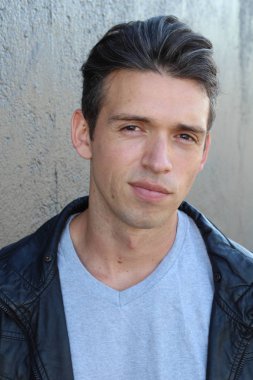 Gri duvarın önünde sıradan giyinmiş yakışıklı bir gencin yakın plan portresi.