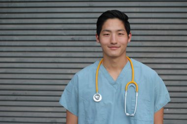 Gri duvarın önünde steteskopu olan yakışıklı Asyalı genç bir doktorun yakın plan portresi.