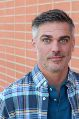 Tuğla duvarın önünde rahat gömlekli, yakışıklı, olgun bir adamın yakın plan fotoğrafı.