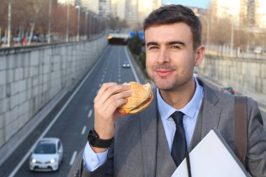 close-up portrait of handsome young businessman in suit eating burger on street