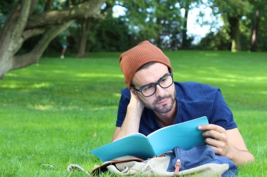 Çimlerin üzerinde yatarken not defteriyle çalışan yakışıklı bir gencin yakın plan portresi.