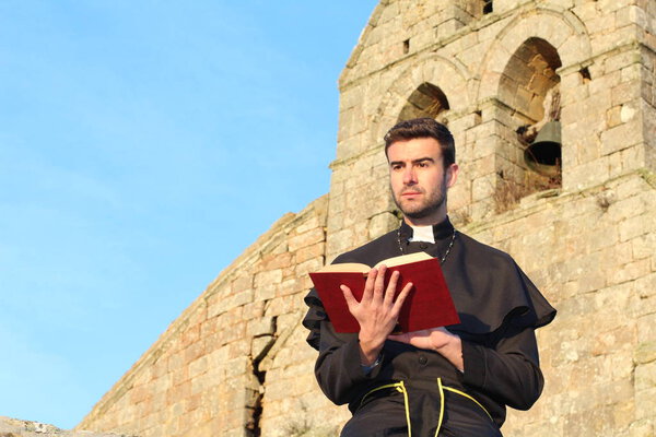 close-up portrait of handsome young priest with holy bible in front of cathedral