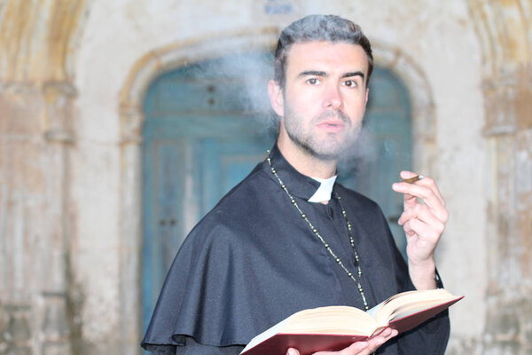 close-up portrait of handsome young priest smoking cigarette in front of cathedral