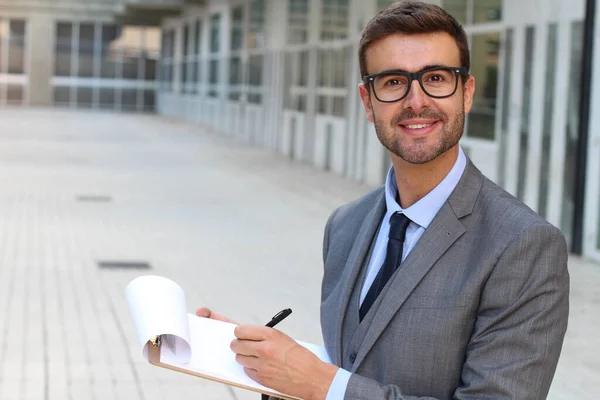 close-up portrait of handsome young businessman writing in clipboard on street