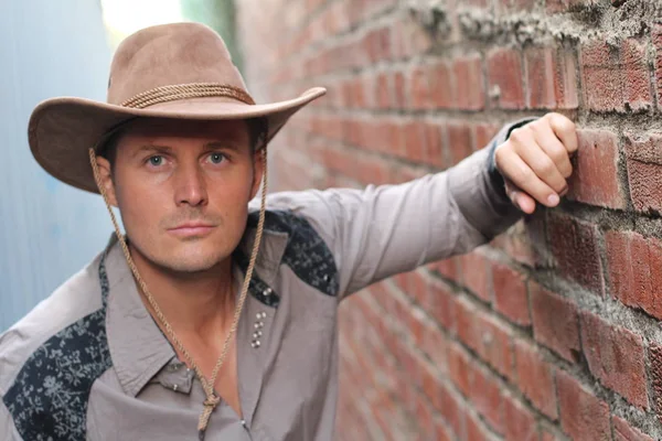 Duvara yaslanmış kovboy şapkalı yakışıklı genç adamın yakın plan portresi.